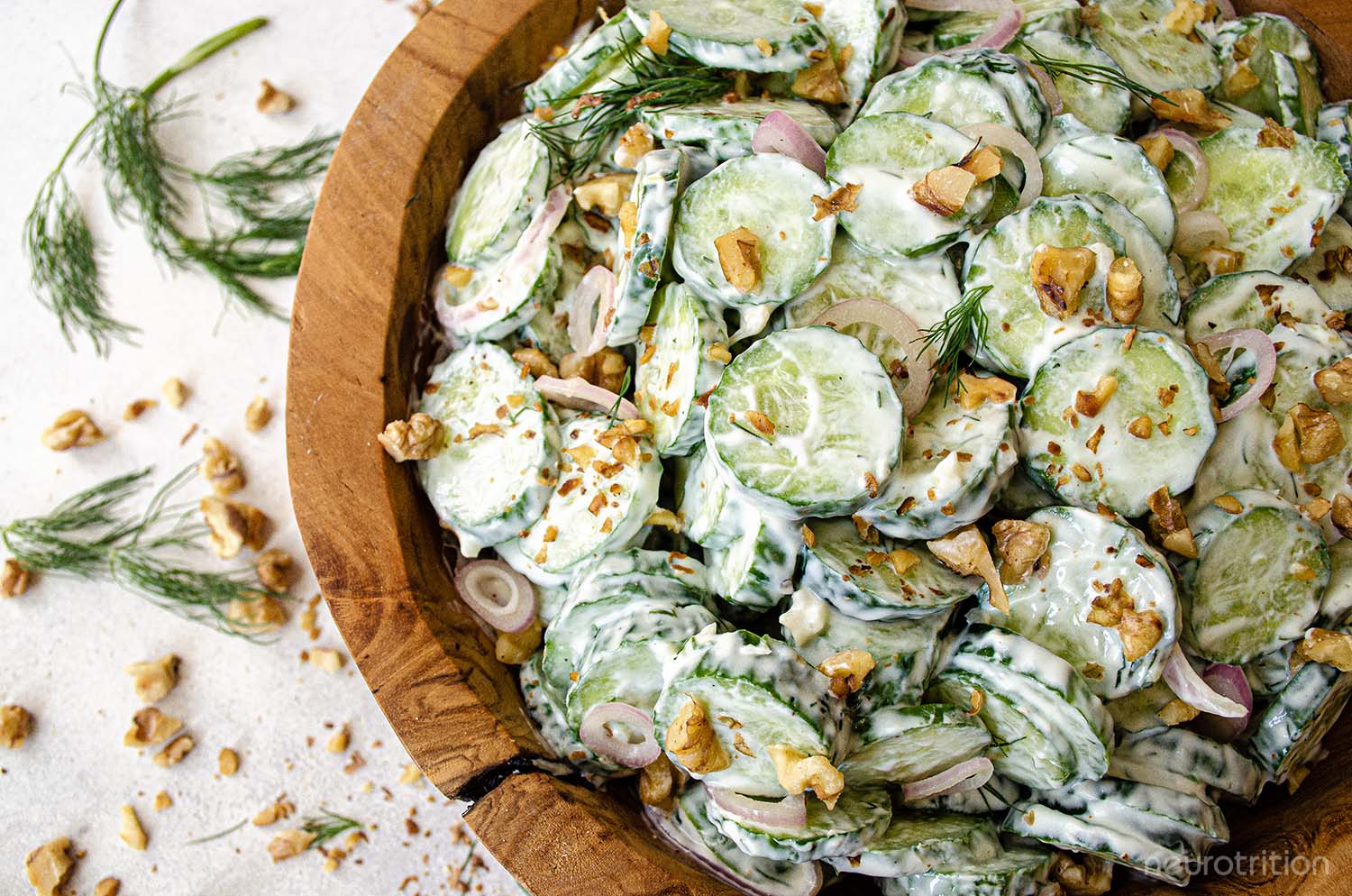 Sliced cucumbers and chopped walnuts in a creamy dressing inside a wooden bowl, topped with dill springs.