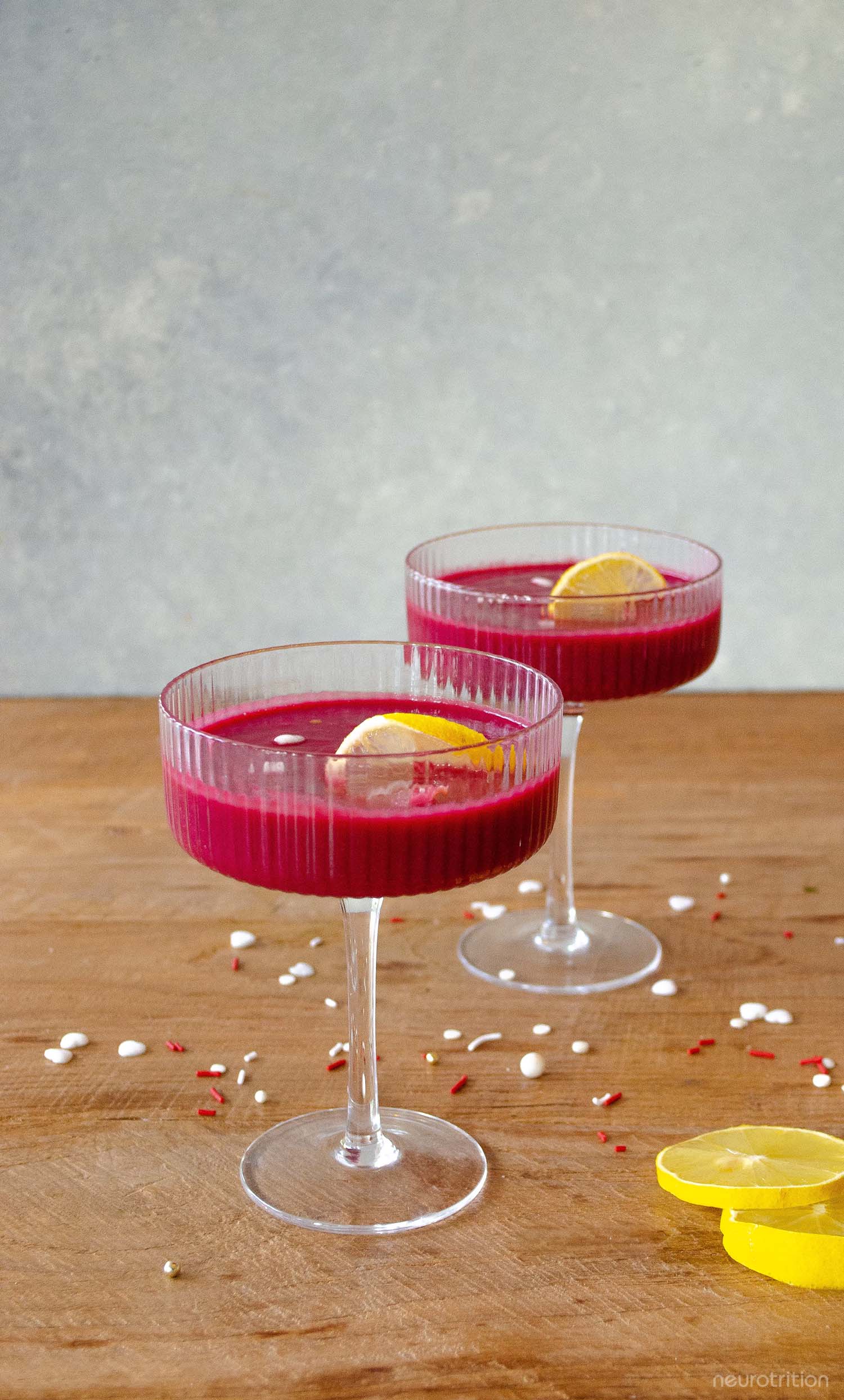 Two bright pink smoothies in cocktail glasses, with lemon twists and heart and star sprinkles.