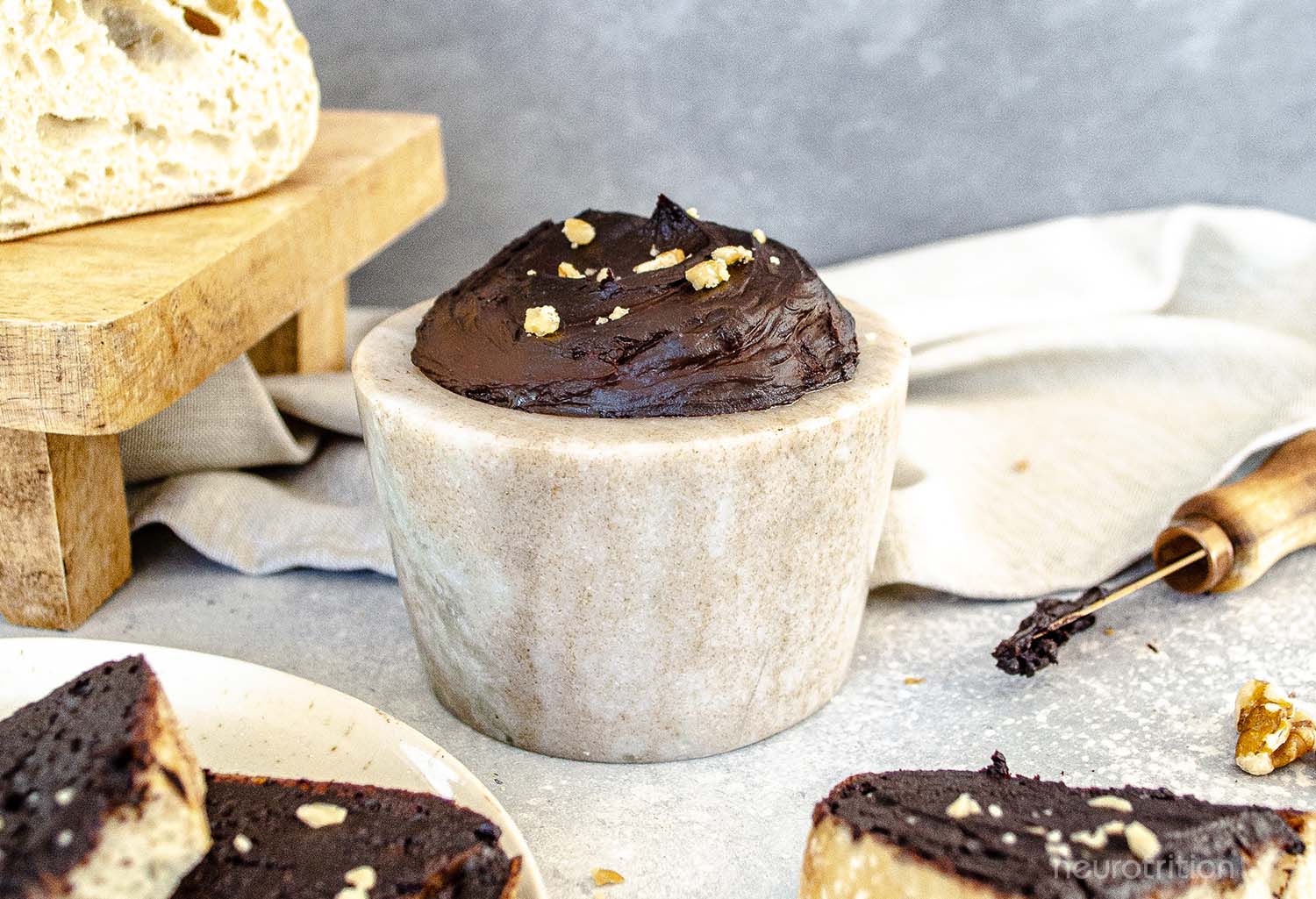 A stone dish full of homemade chocolate spread is surrounded by slices of bread that are covered in the chocolate spread and topped with crushed walnuts.