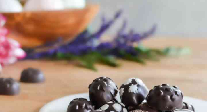 A pile of homemade chocolate Easter eggs with decorative white icing, on a white plate.