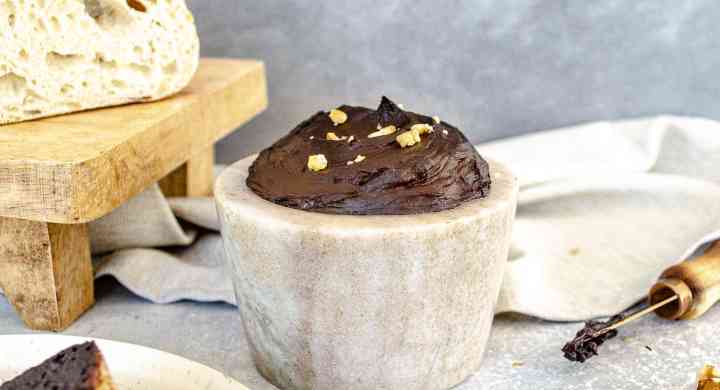 A stone dish full of homemade chocolate spread is surrounded by slices of bread that are covered in the chocolate spread and topped with crushed walnuts.